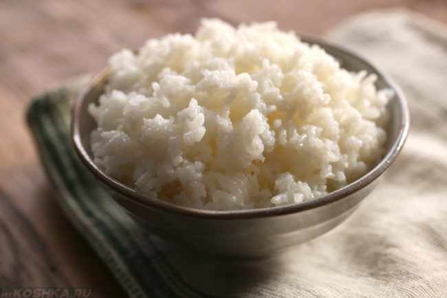 Сваренный белый рис в глубокой тарелке на полотенце