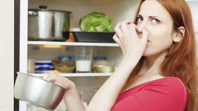 Женщина у открытого холодильника и закрывающая нос при испорченном продукте